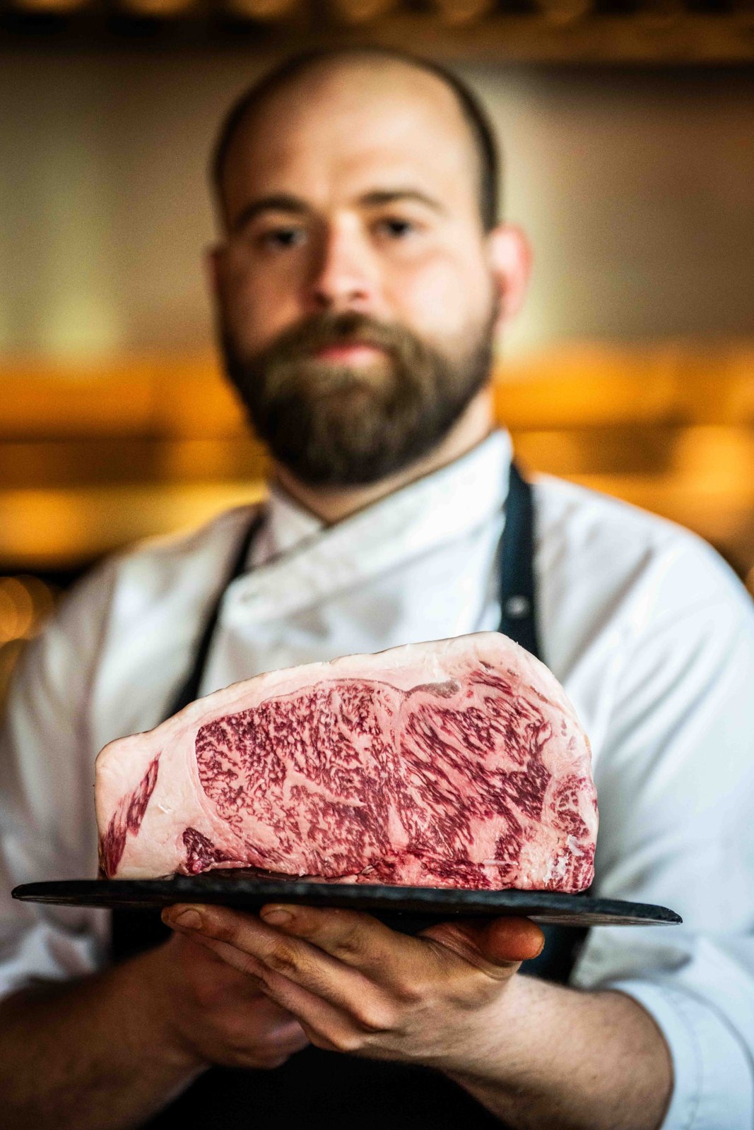 Chef toont een zwaar gemarmerde ribeye op een leisteen plateau